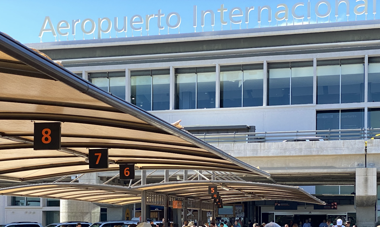 Private SUV and shared shuttle van waiting outside airport terminal with passengers loading luggage - cabo san lucas international airport