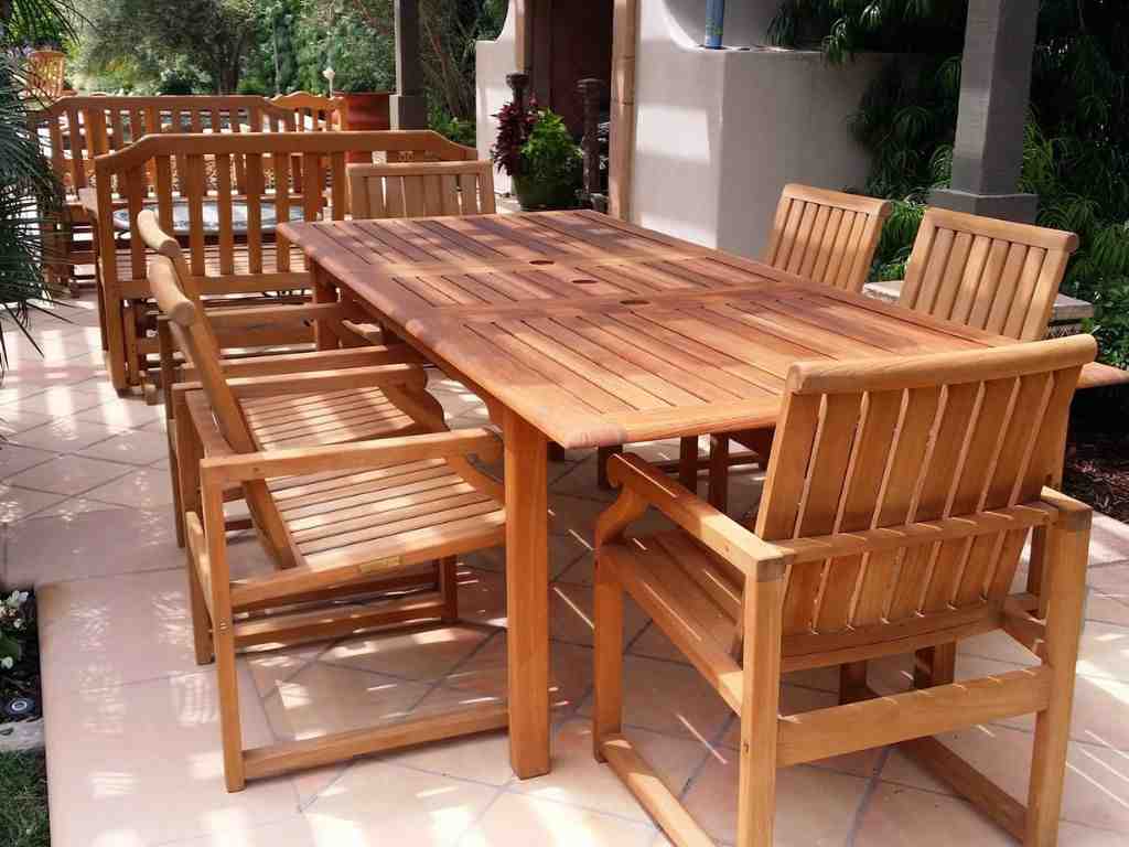 Outdoor wooden dining table with matching chairs arranged on a covered patio.
