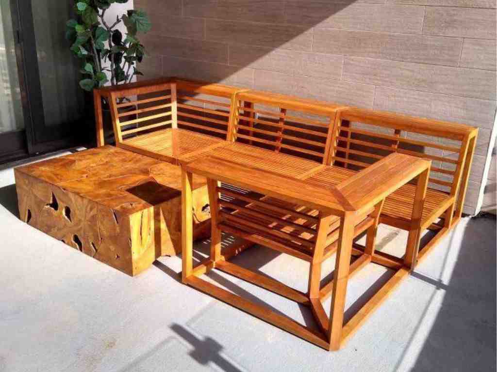 Wooden patio dining set with bench seating and a rectangular table beside a carved wooden storage chest on a sunlit balcony.