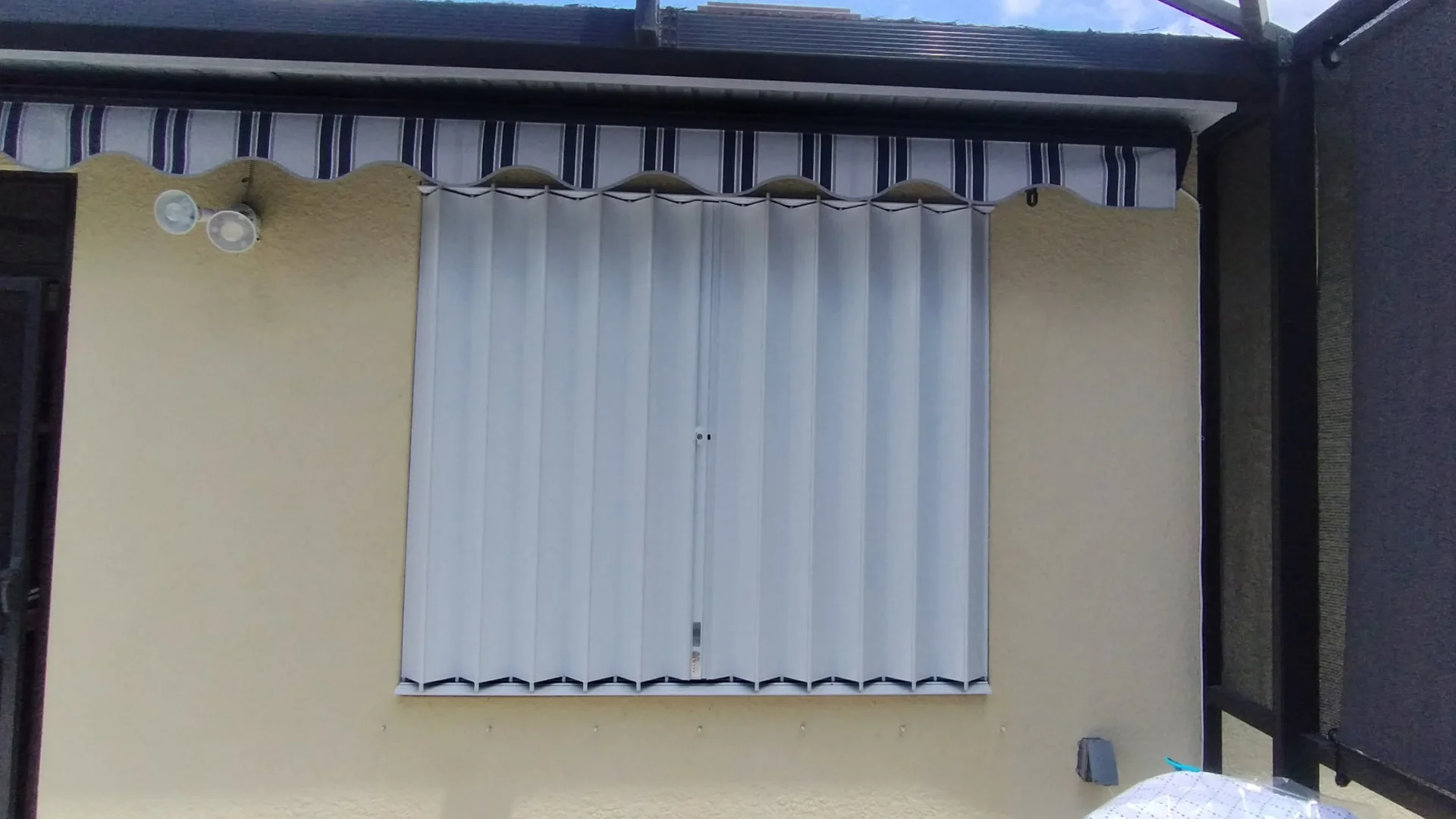 White accordion storm shutters closed over a window on a Florida home White accordion storm shutters closed over a window on a Florida home