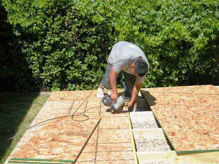 A worker securing the floor panels of a DIY storage shed, an important step in building your own storage shed.