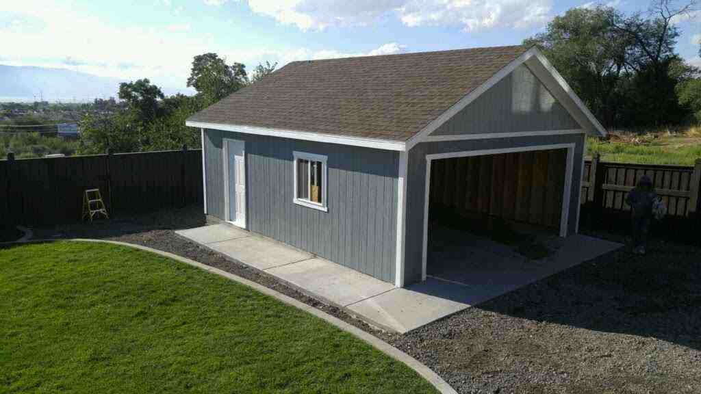 A custom detached garage featuring cedar shake gables, a clean design, and surrounding landscape.