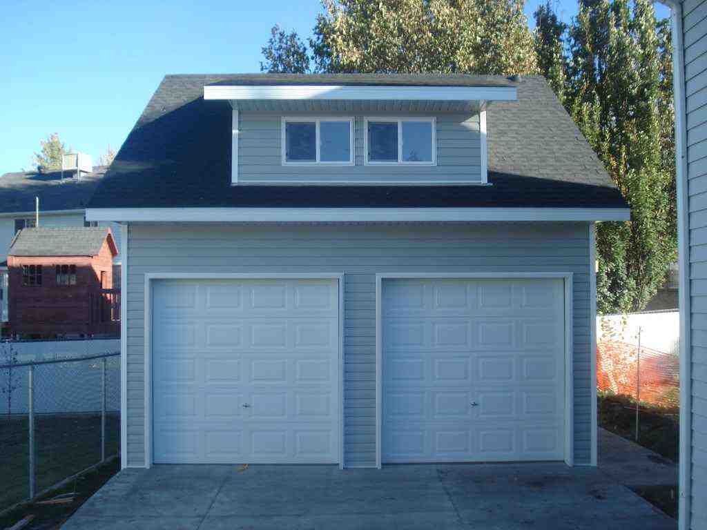 A custom two-car garage with a dormer, featuring a stylish roof and clean exterior design.