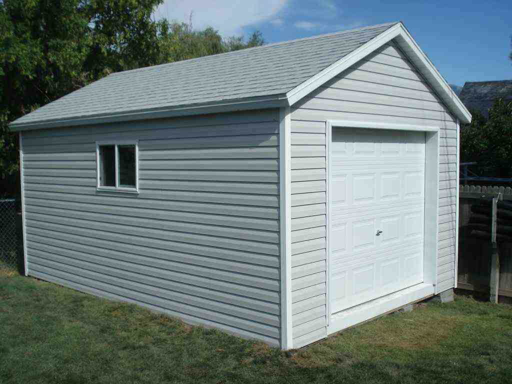 A small gray detached garage with white trim, gable roof, single door, and side window in a backyard.
