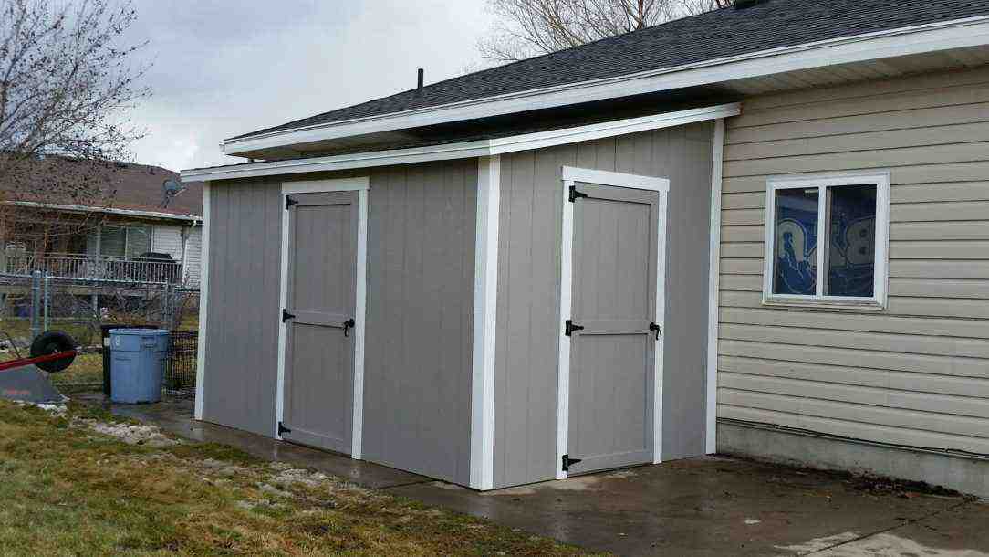 Freshly painted gray lean-to shed with white trim – clean and practical lean-to shed painting beside house.