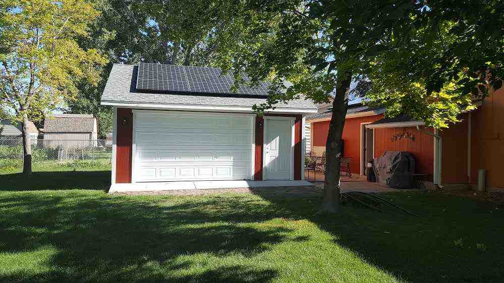 A custom garage featuring solar panels on the roof, located in a green backyard setting.