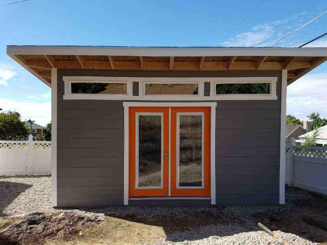 Gray modern shed with orange French doors and lean-to roof; great example of backyard studio exterior painting.