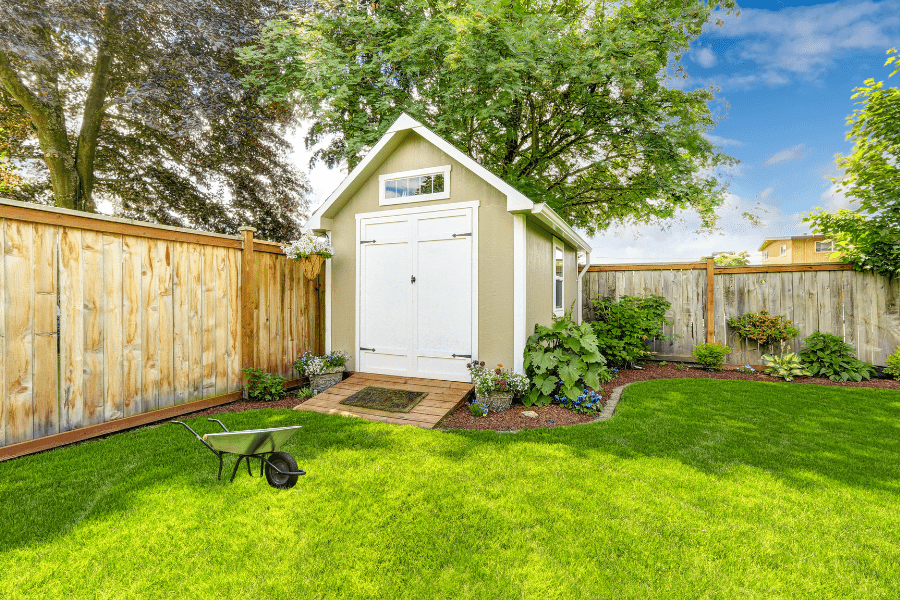 A light green shed with an entry ramp, surrounded by a well-maintained garden. Focus on shed entry ramp solutions.