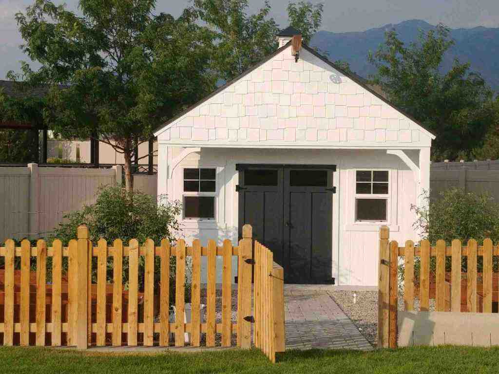 Orchard Shed with Shake Shingle Gable Design Orchard shed with shake shingle gable, white siding, black double doors, and front fence, designed for backyard storage and orchard use.
