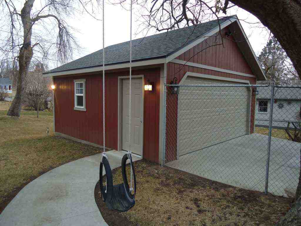 Red detached garage with beige trim, side door entry, and chain-link fence beside a tree and yard swing.