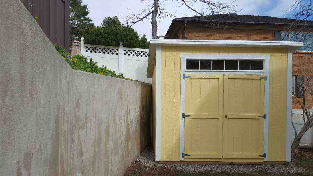 A completed lean-to shed in Salt Lake with yellow paint and double doors, placed beside a concrete wall.