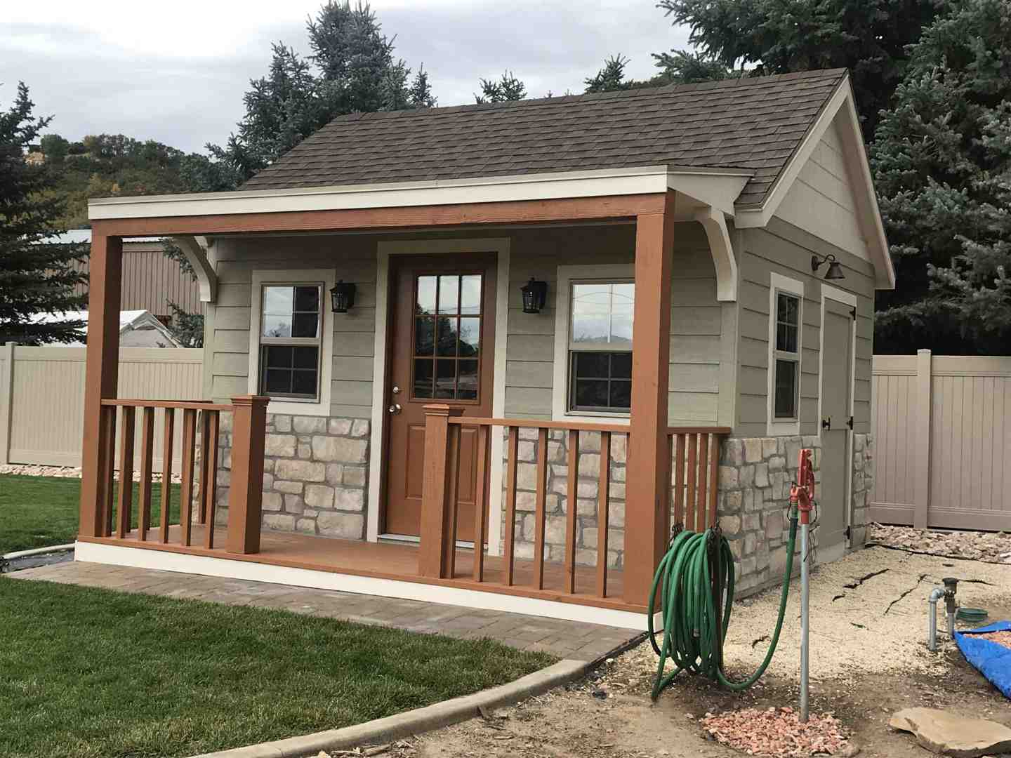 Green ranch style wood shed with porch, stone siding, and brown trim – focus keyword: ranch style wood shed.