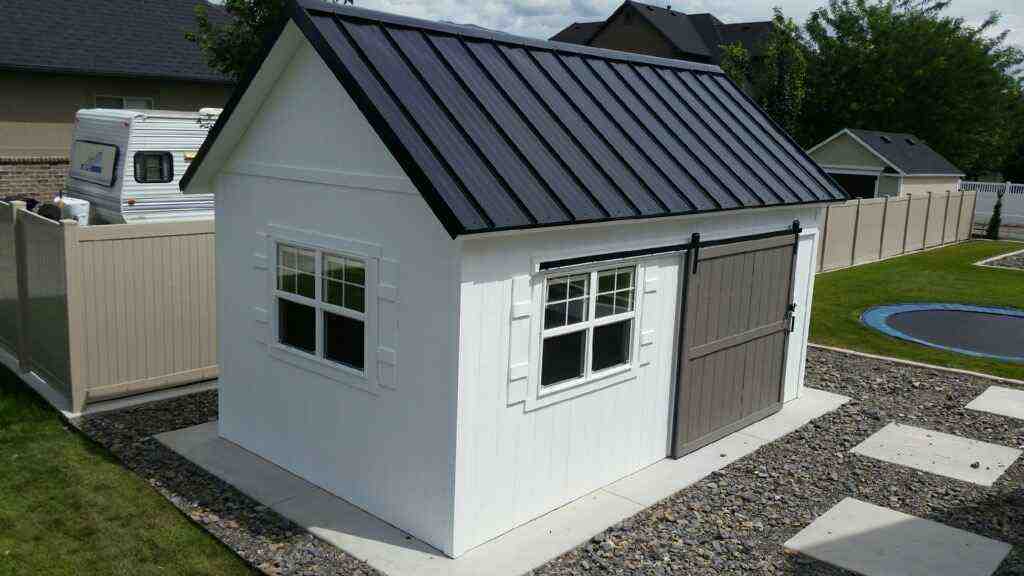 Stylish orchard shed featuring a black metal roof and sliding barn door, built to meet Utah shed building code.