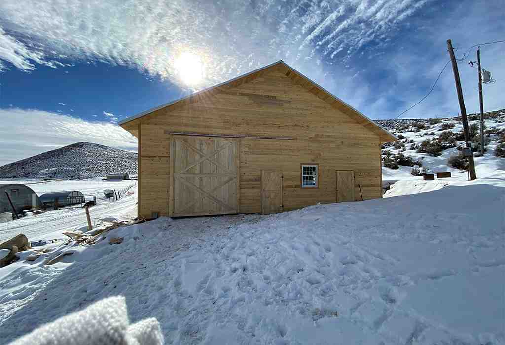 Wood Farm Shed Built for Winter Conditions Wood farm shed built in a snowy rural setting, showing materials, size, and design factors that affect the cost of building a farm shed.