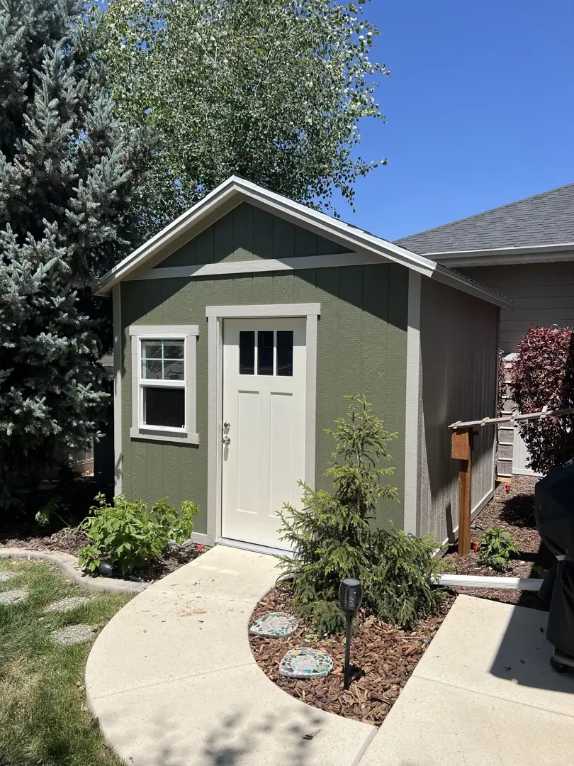 Custom Backyard Storage Shed Green custom backyard storage shed with white trim and window set along landscaped concrete walkway in residential yard