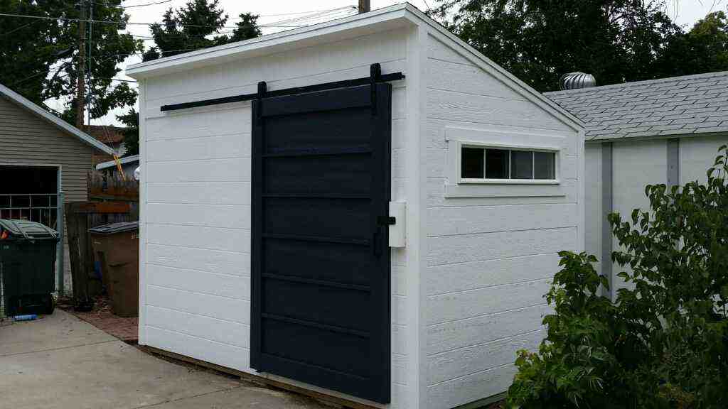  A sleek white custom lean-to storage shed with a black sliding door, offering stylish storage solutions.