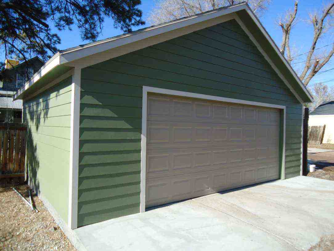 Green detached garage with smooth lap siding, beige double garage door, and gable roof in a residential yard.