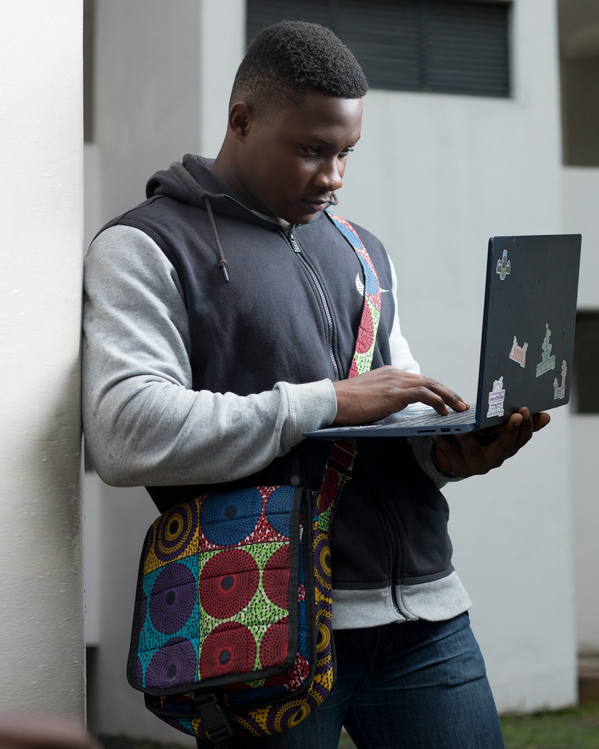 A student standing outside, laptop balanced on one hand, typing with the other.
