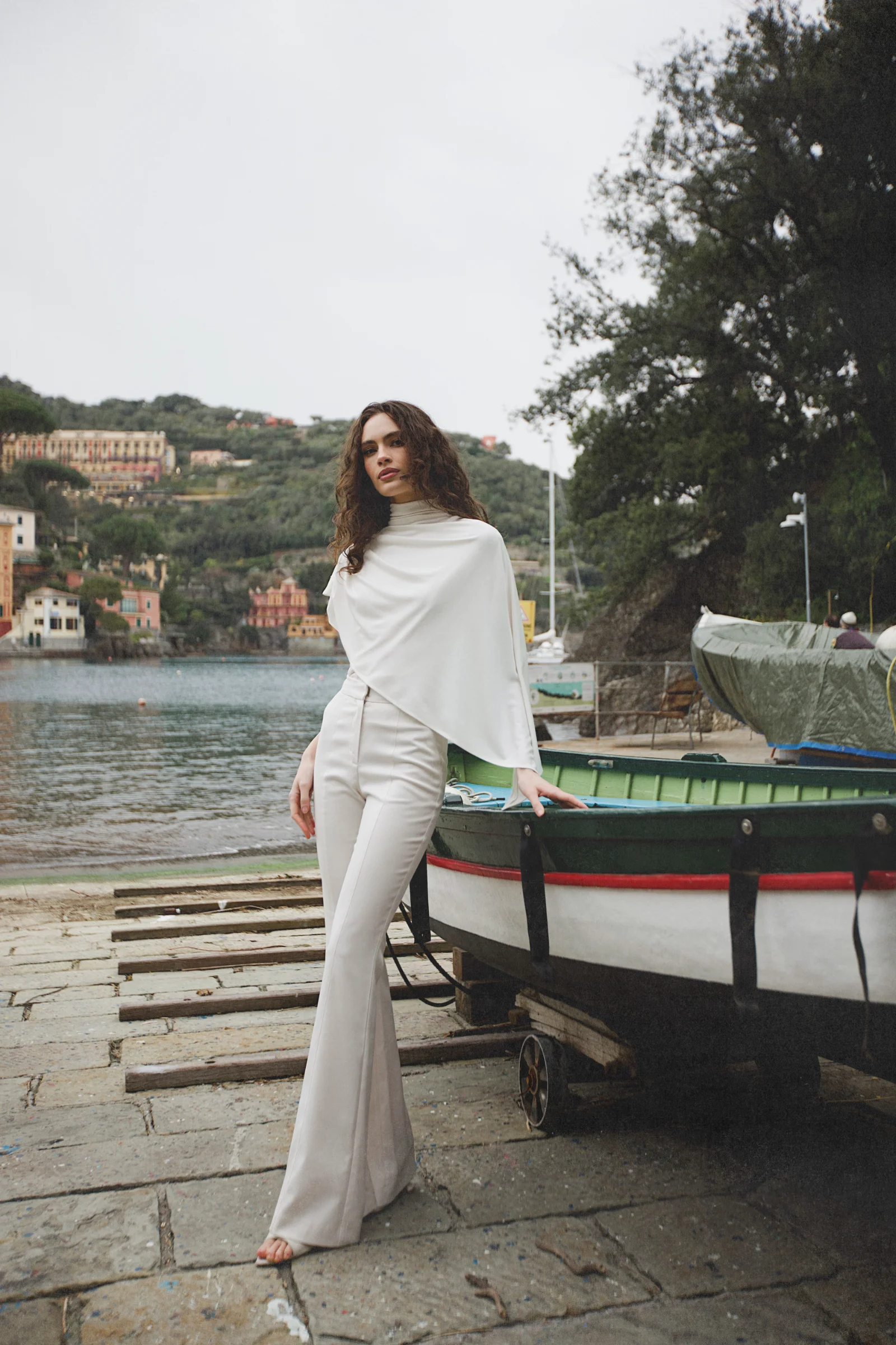 White asymmetric designer top with high neck, integrated cape, and fluid draping 