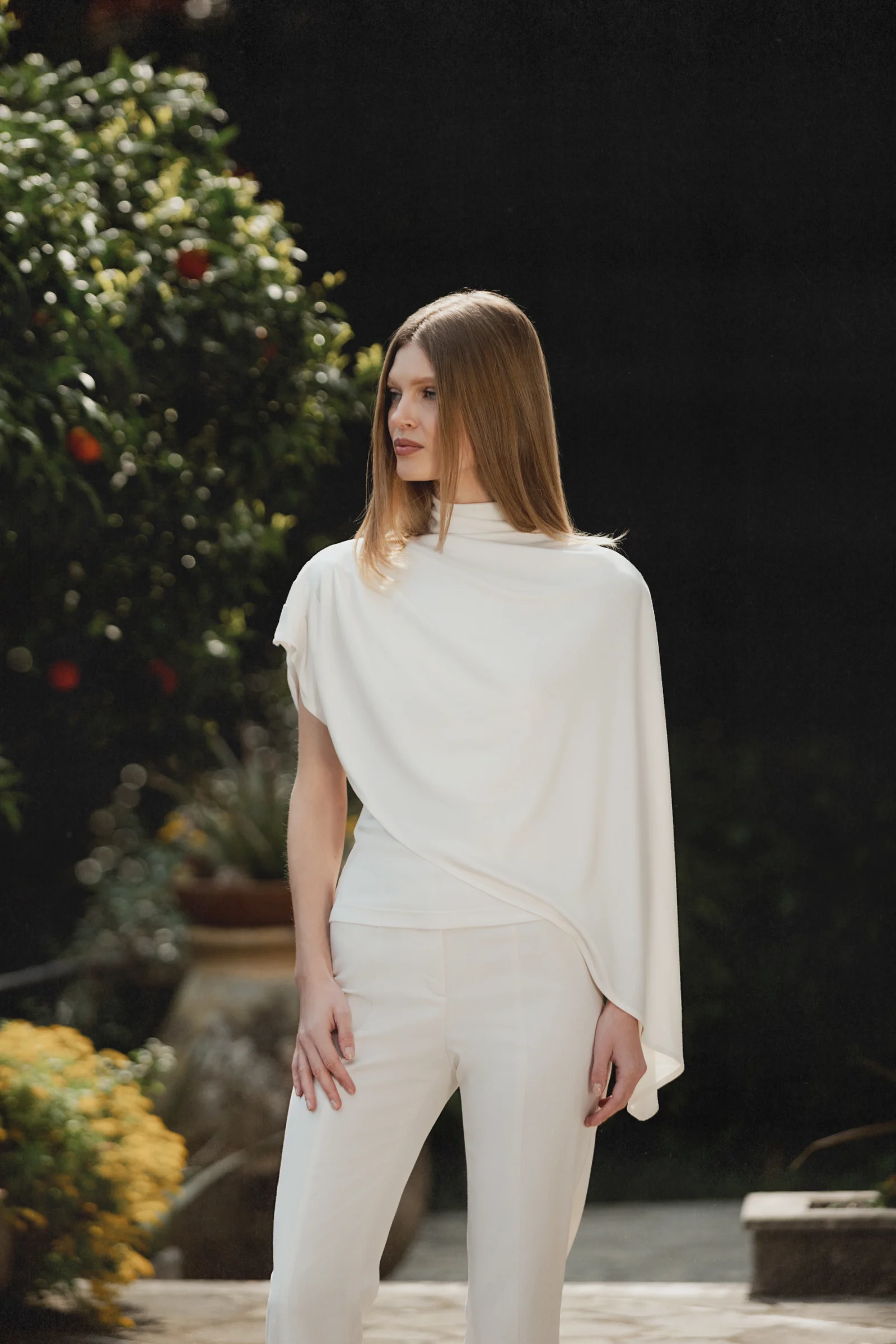 White asymmetric designer top with high neck, integrated cape, and fluid draping 