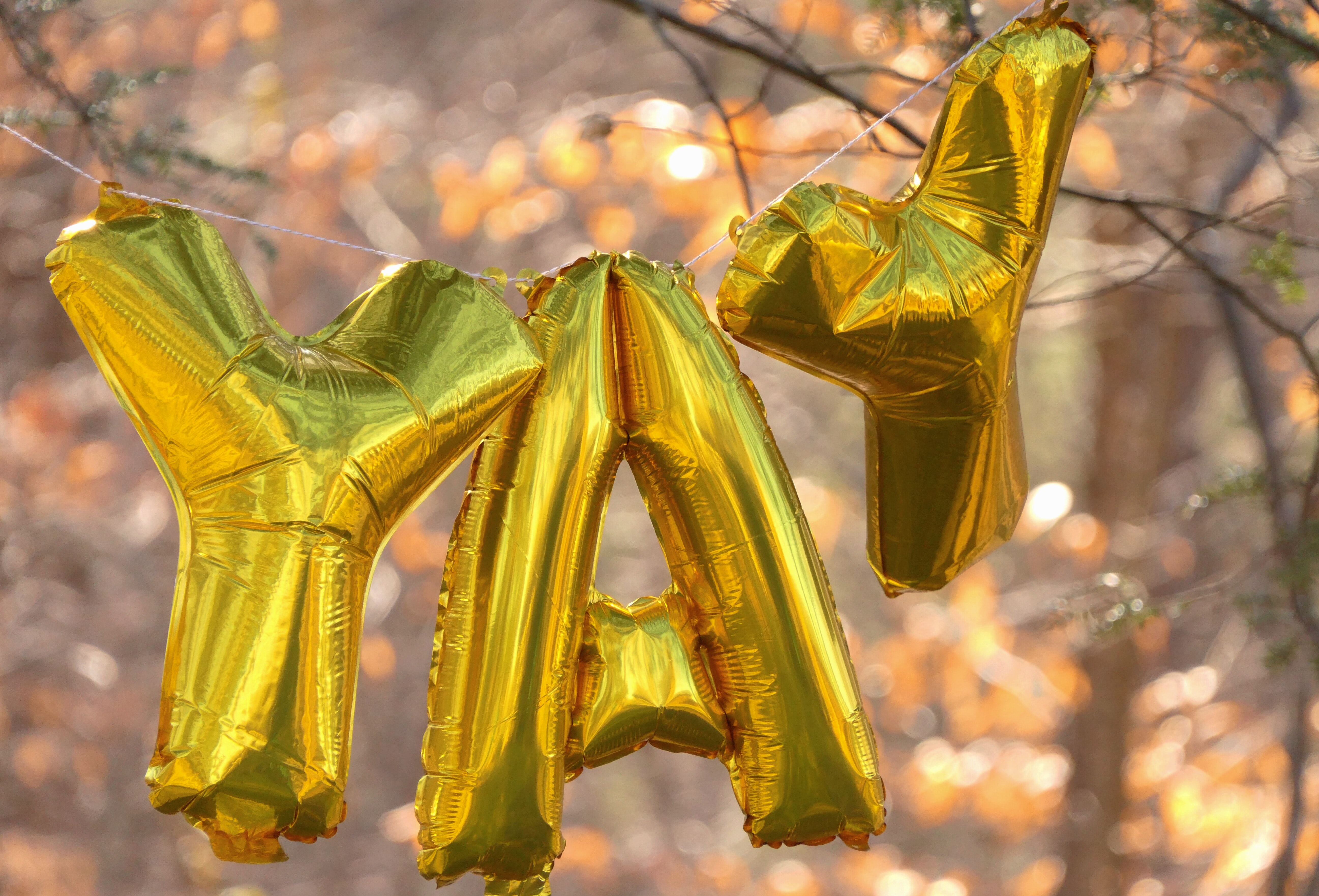 Gold foil balloons spell the word YAY while suspended from a string in the sunshine