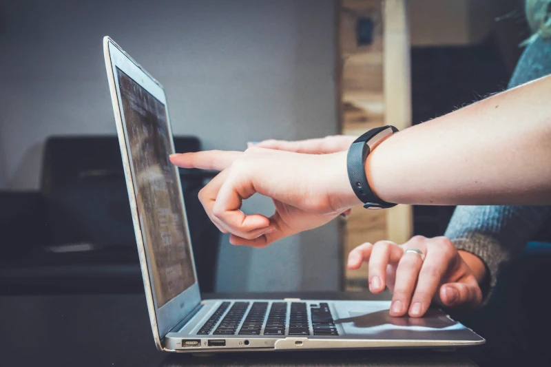 Two people pointing at a laptop screen while another works with the trackpad