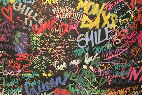 Black surface covered in layers of text graffiti with words like Smile, Game On, Chill!!, and Love coming to the surface against a wide range of text styles and colors.