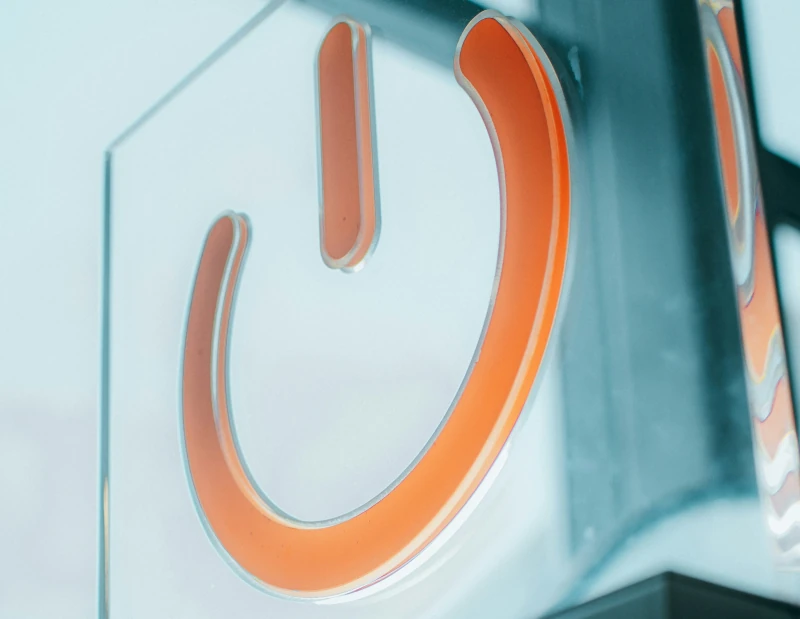 Large orange power symbol (semi-circle facing up with a line through the center) on a glossy surface reflecting the sky through a window.