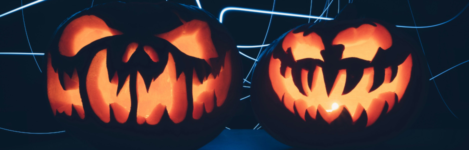 Two scary-looking jack-o'-lanterns glowing orange from the inside against a dark slightly blue background with pale blue streaks of light.