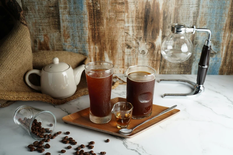 Setup to brew coffee with a siphon, beakers, and a spoon, with coffee beans scattered around.