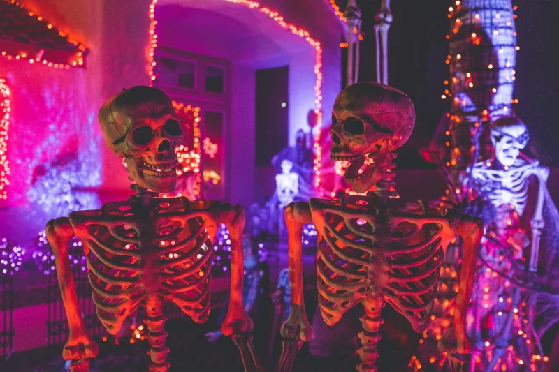 2 skeletons talking to each other, one of the them laughing while at a halloween party