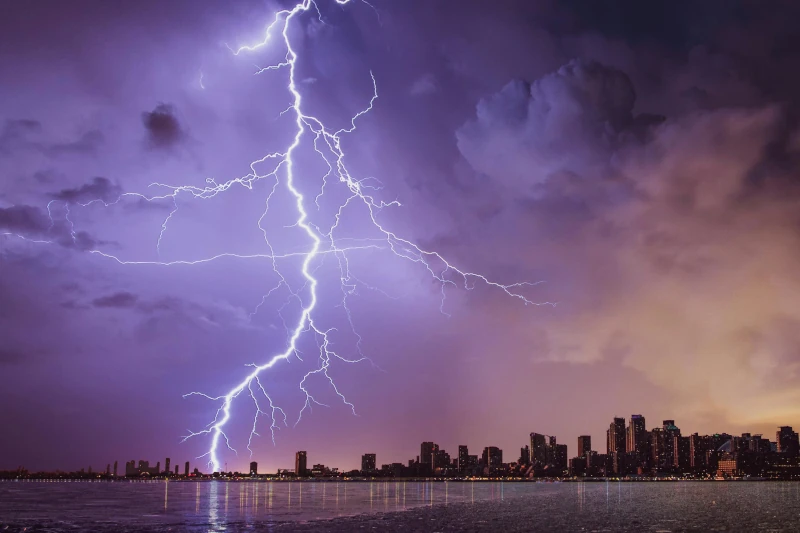 A lightning bolt strikes down from the purple sky and strikes a building in a coastal city.