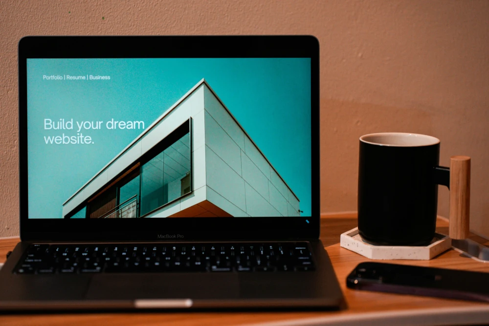 Laptop showing a web page about building a dream website. On the desk with the laptop is a phone and coffee mug.