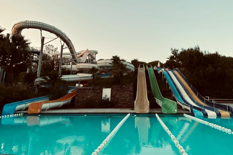 Water park with 7 water slides coming down a hill and ending in the same pool with teal colored water.