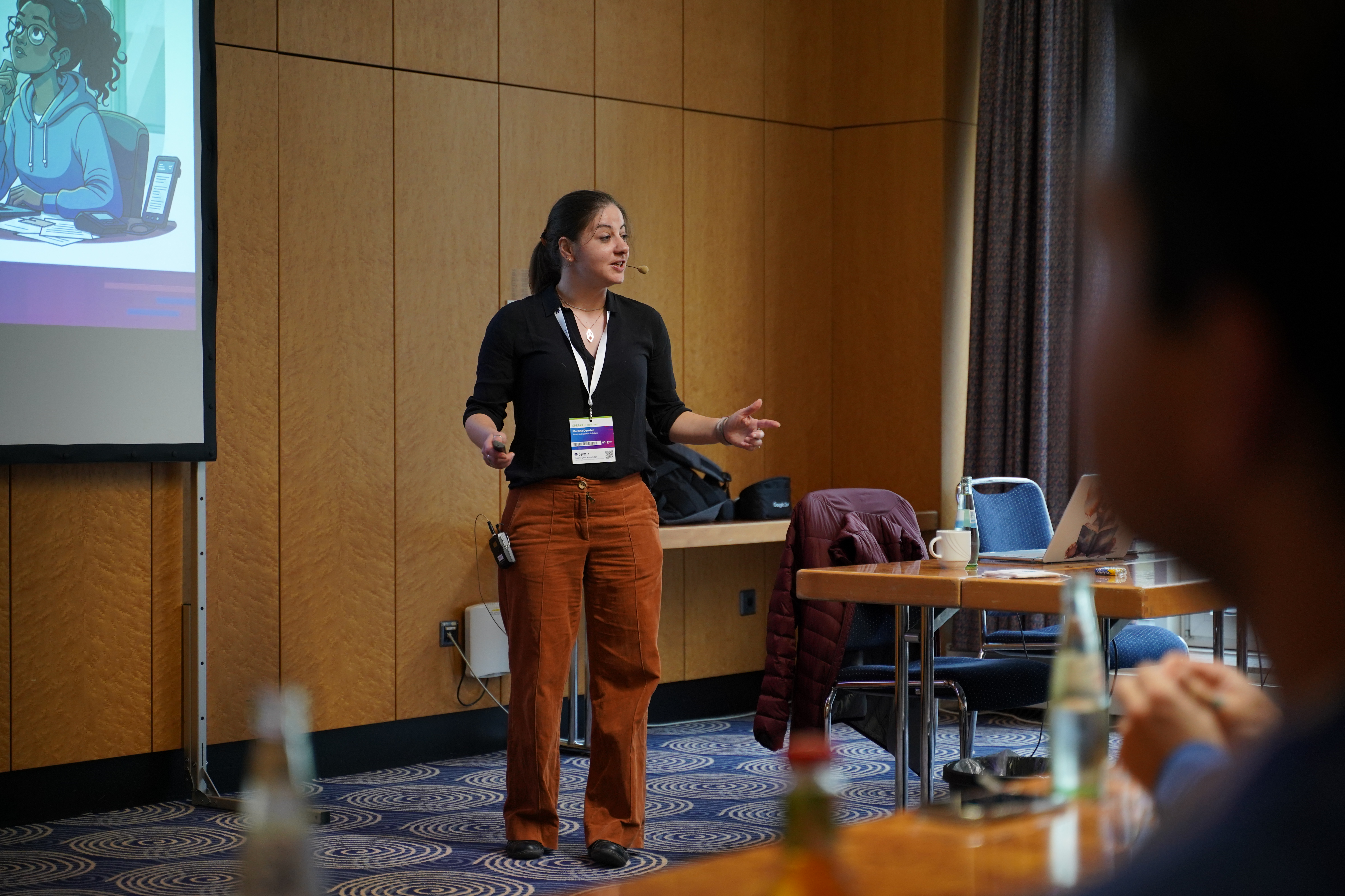 Martine Dowden, in rust colored pants and a black top, speaking in front of an audience.