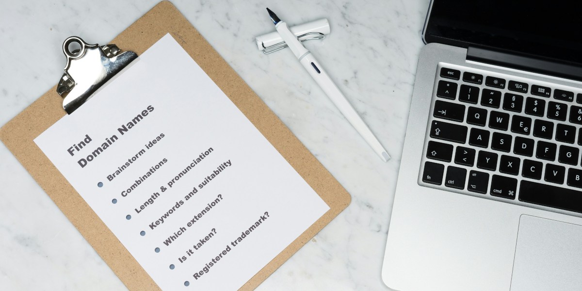 A laptop sitting on a desk beside a pen and clipboard. The clipboard has a sheet of paper listing qualifications for finding domain names: brainstorm ideas, combinations, length and pronunciation, keywords and suitability, which extension, is it taken, registered trademark.