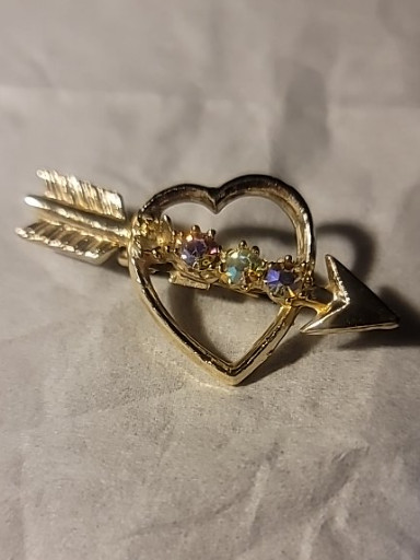 Gold-tone metal brooch featuring a heart pierced by an arrow, set with aurora borealis rhinestones