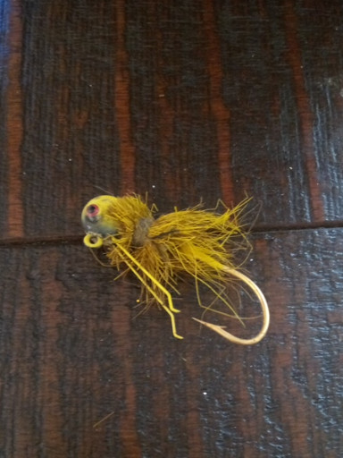 Hand-tied fly fishing lure in olive/yellow, likely a dragonfly nymph or crayfish pattern