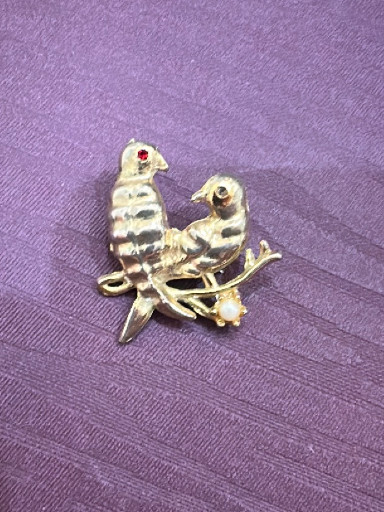 Gold-tone metal brooch depicting two birds perched on a branch with red rhinestone eyes