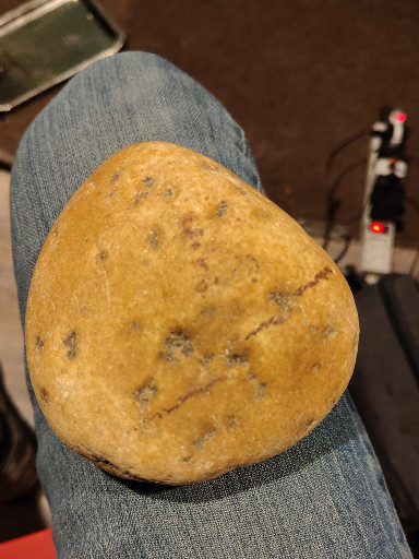 Natural river rock or decorative stone with golden-yellow coloration and dark mineral inclusions