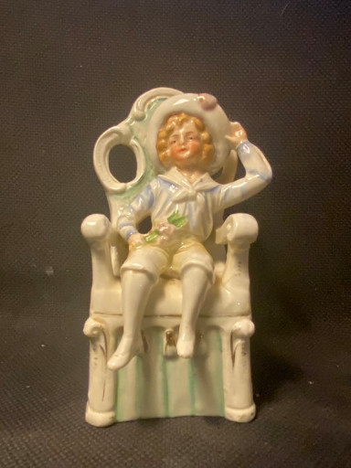 Porseleinen biscuit beeldje van een Victoriaanse jongen zittend op een stoel