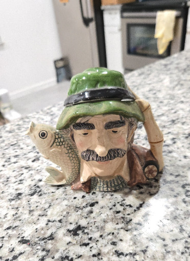 Ceramic character jug depicting a fisherman with green hat and fish handle