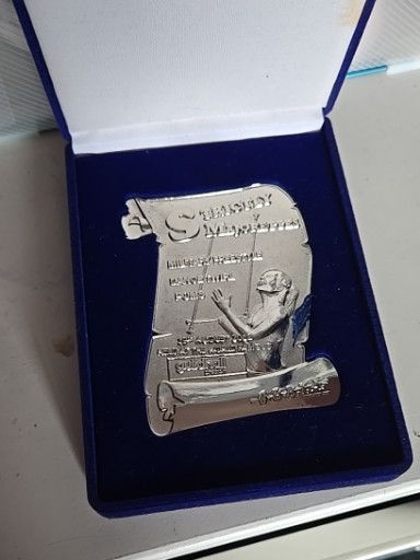 Silver-plated commemorative plaque or medal featuring a figure at a desk with typewriter