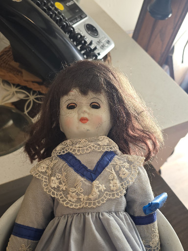 Cloth doll with porcelain or composition face, dressed in traditional gray dress with lace trim and blue ribbon accents