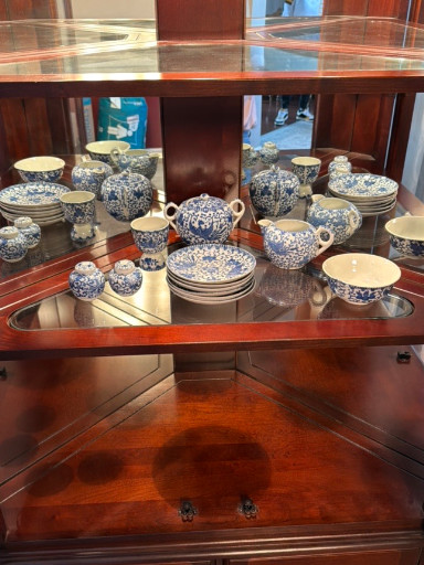 Mahogany corner china cabinet with glass shelves displaying blue and white porcelain collection