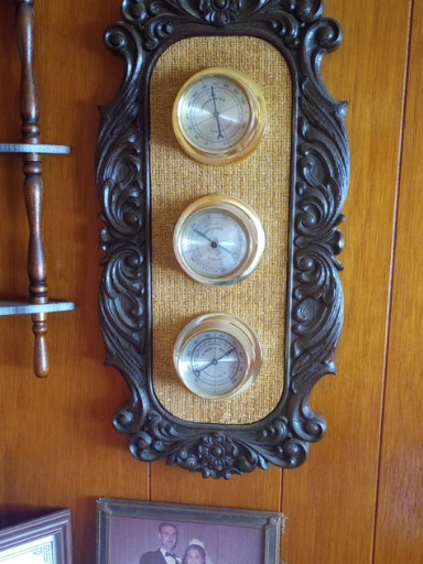 Vintage wall-mounted weather station with barometer, thermometer, and hygrometer in ornate carved wood frame