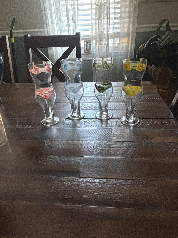 Set of four clear glass goblets with colored water (pink, blue, green, yellow)