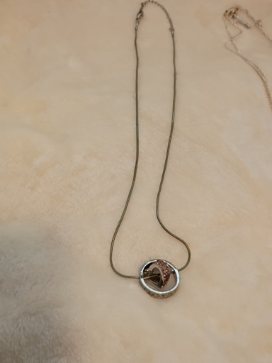 Sterling silver necklace with circular pendant featuring copper-toned heart and cubic zirconia accent