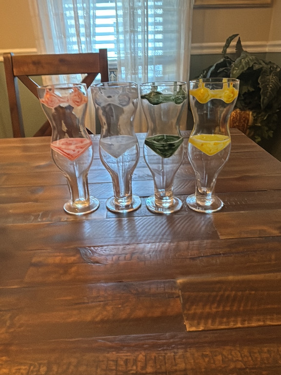 Set of four novelty drinking glasses featuring male and female nude torso designs in pink, blue, green, and yellow