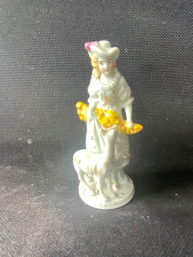 Porselein beeldje van een vrouw in 18e-eeuwse kledij met gele bloemen